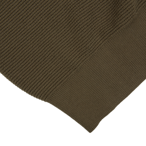 A close up of a Sunspel khaki green cotton waffle stitch crew neck sweater on a black background.