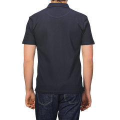 Rear view of a person in a Sunspel Midnight Blue Cotton Riviera Polo Shirt and jeans, standing against a plain background.