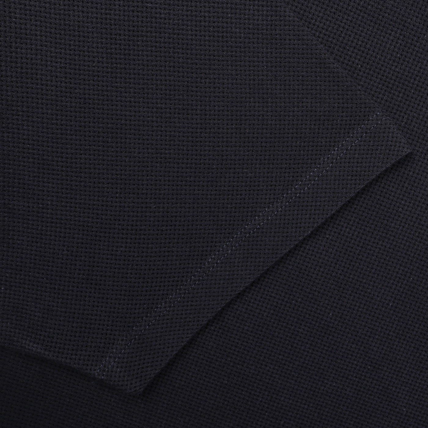 Close-up of a Midnight Blue Cotton Riviera Polo Shirt by Sunspel, featuring a waffle texture and intersecting seams. Crafted from breathable cotton mesh, this versatile staple blends comfort and style effortlessly.