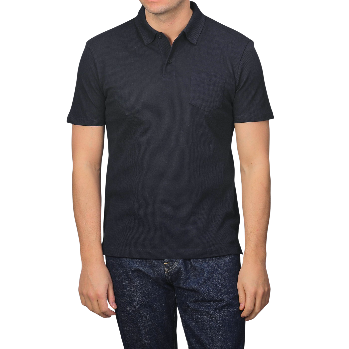 A person wears a Sunspel Midnight Blue Cotton Riviera Polo Shirt and blue jeans against a plain backdrop, highlighting this versatile staple made from breathable cotton mesh.