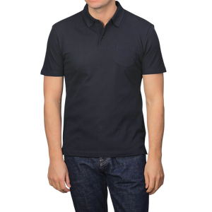 A person wears a Sunspel Midnight Blue Cotton Riviera Polo Shirt and blue jeans against a plain backdrop, highlighting this versatile staple made from breathable cotton mesh.