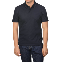 A person wears a Sunspel Midnight Blue Cotton Riviera Polo Shirt and blue jeans against a plain backdrop, highlighting this versatile staple made from breathable cotton mesh.