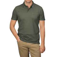 Dressed in a Sunspel Pine Green Cotton Riviera Polo Shirt with a chest pocket, paired with beige pants, one casually slips a hand in a pocket, epitomizing the contemporary and sophisticated style of its breathable cotton fabric.