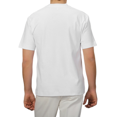 A person wearing Sunspel's White Supima Cotton Relaxed Fit T‑shirt with light-colored pants is shown from the rear against a gray background.