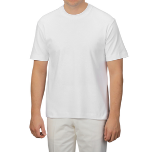 A person poses effortlessly against a neutral background, wearing a Sunspel White Supima Cotton Relaxed Fit T-shirt and matching pants, showcasing style and comfort.