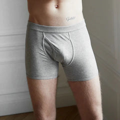 A person wearing Grey Melange Pima Cotton Wil Trunks by The White Briefs stands indoors, their upper body not fully visible.