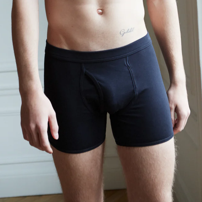 A person stands wearing The White Briefs Parisian Night Pima Cotton Wil Trunks, displaying a tattoo above the waistband. Only the torso and upper legs are visible.