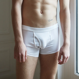 A person standing indoors wearing The White Briefs' White Pima Cotton Elm Short Briefs, with a tattoo visible on their left side.
