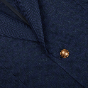 Close-up of a Navy Blue Herringbone Cotton Linen Vesuvio Blazer fabric with a structured pattern and a small gold button by Tagliatore.
