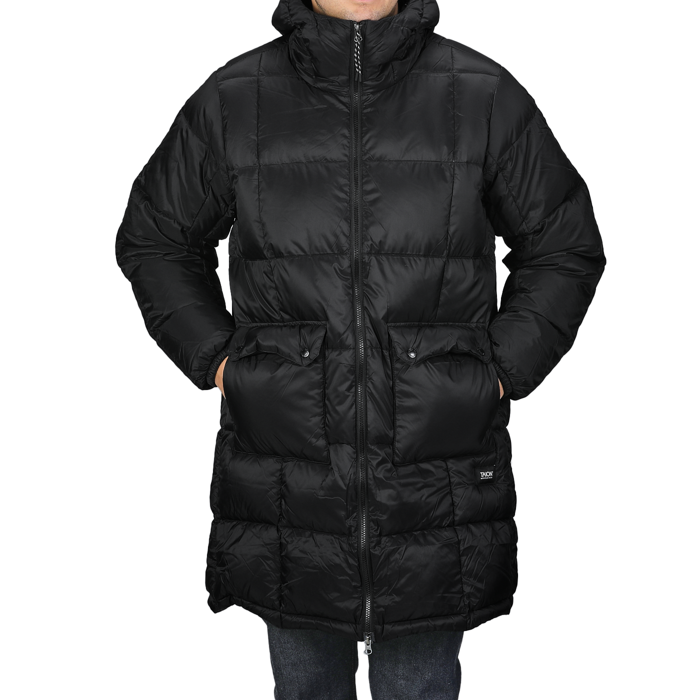 A person is wrapped in a Black Nylon Down Padded Parka by Taion, featuring a long, quilted design with pockets and a high collar, made from durable nylon outer material.