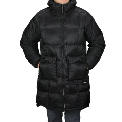 A person is wrapped in a Black Nylon Down Padded Parka by Taion, featuring a long, quilted design with pockets and a high collar, made from durable nylon outer material.