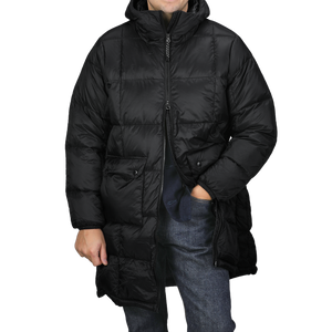 A person is wearing the Taion Black Nylon Down Padded Parka, with its hooded design and durable nylon exterior. Their hands are tucked into the jacket’s pockets, and the parka is zipped up to provide both comfort and style.