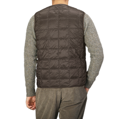 A person is shown from the back wearing a Taion Dark Chocolate Nylon Down Padded Vest over a gray sweater, with its high-density nylon exterior subtly hinting at its comfort.