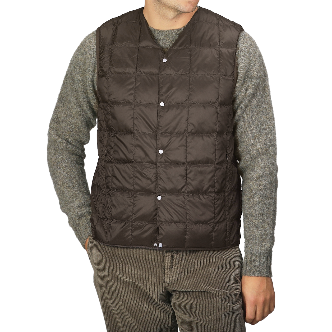 A person wearing a Taion Dark Chocolate Nylon Down Padded Vest over a gray sweater and brown corduroy pants, with hands in pockets.