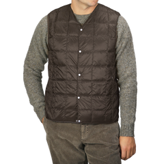 A person wearing a Taion Dark Chocolate Nylon Down Padded Vest over a gray sweater and brown corduroy pants, with hands in pockets.