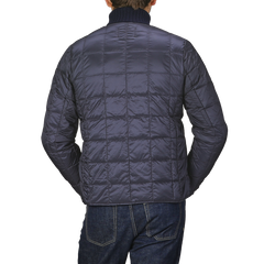 A person is depicted from behind clad in a Navy Blue Nylon Down Padded Jacket by Taion, paired with dark jeans, and set against a gray background.