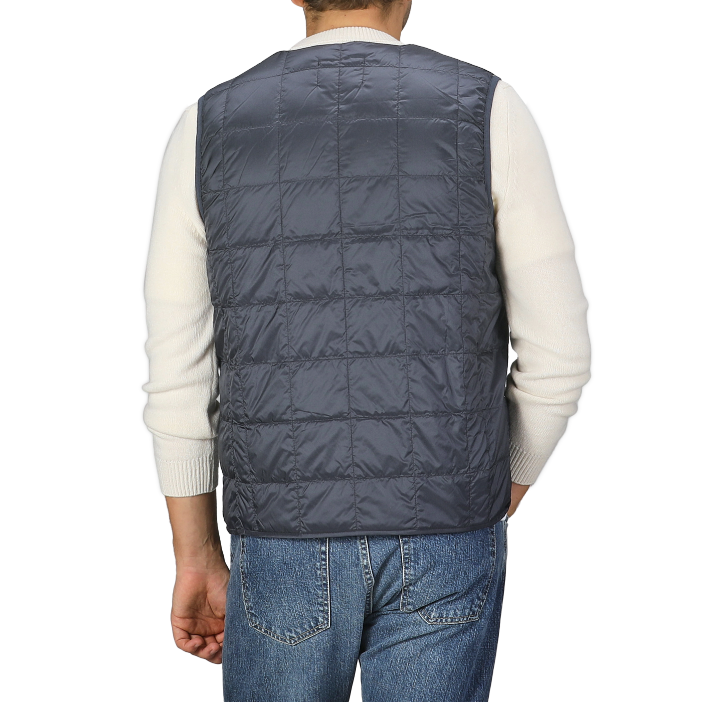 A person wearing a navy blue nylon down padded vest from Taion over a white long-sleeve shirt and blue jeans, seen from the back.