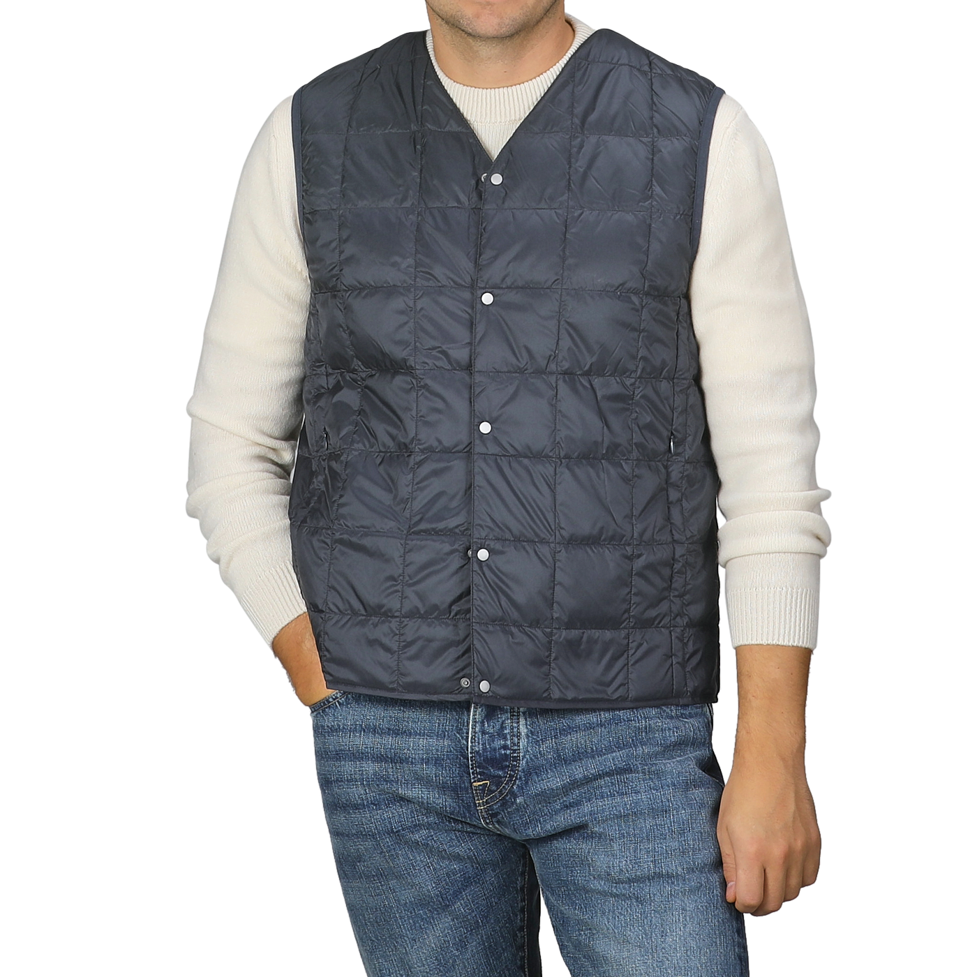 A man is wearing the Taion Navy Blue Nylon Down Padded Vest over a white sweater and blue jeans, standing against a plain background. The vest’s high-density nylon material adds an element of sophistication to his look.