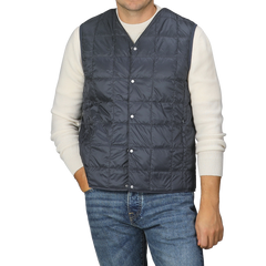 A man is wearing the Taion Navy Blue Nylon Down Padded Vest over a white sweater and blue jeans, standing against a plain background. The vest’s high-density nylon material adds an element of sophistication to his look.