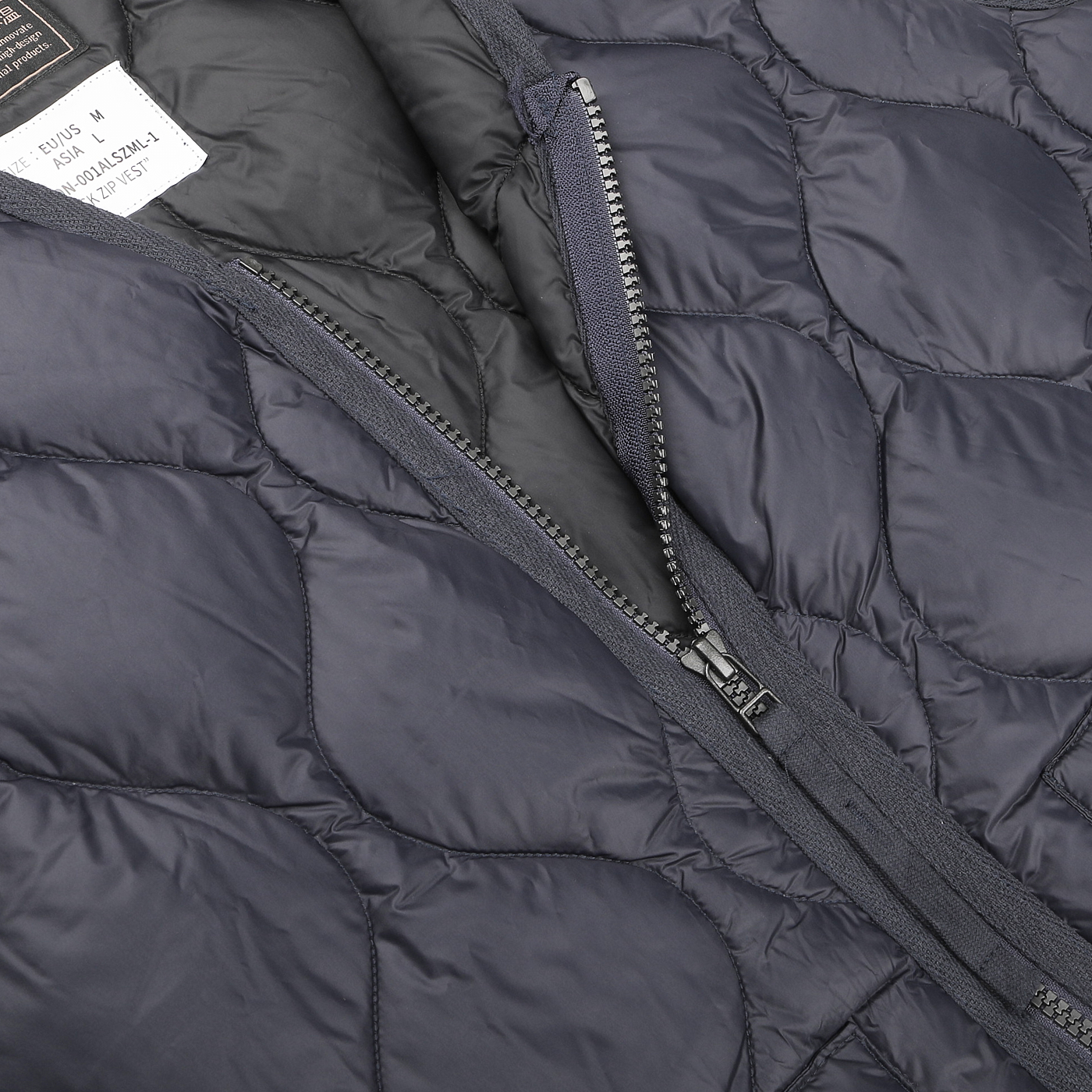 Close-up of a Navy Blue Nylon Down Padded Zip Vest by Taion, featuring a partially open zipper that reveals a white interior label, highlighting the exceptional craftsmanship of Japanese outerwear.