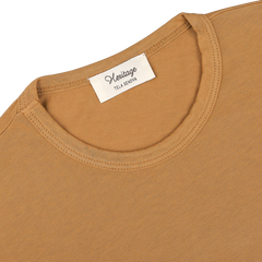 Close-up of a brick orange, heavy organic cotton long sleeve t-shirt with a white label at the collar that reads "Heritage" and "Tela Genova.