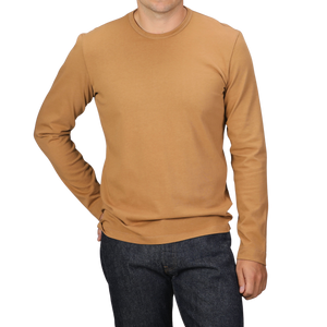 A person wearing a Brick Orange Heavy Organic Cotton Long-Sleeve T-Shirt by Tela Genova and dark jeans stands against a black background.