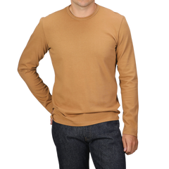 A person wearing a Brick Orange Heavy Organic Cotton Long-Sleeve T-Shirt by Tela Genova and dark jeans stands against a black background.