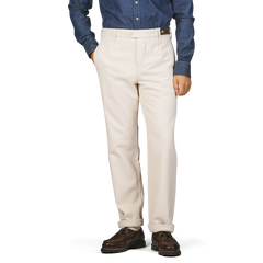 A person dressed in Tela Genova's Ecru Beige Cotton Wool Berardo Trousers, a blue denim shirt, and brown shoes stands with hands in pockets against a plain background.