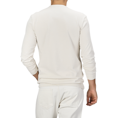 An individual is depicted from the back, attired in an Ecru White Heavy Organic Cotton Long-Sleeve T-Shirt by Tela Genova and white pants. The grey backdrop highlights the simplicity and vintage appeal of the outfit.