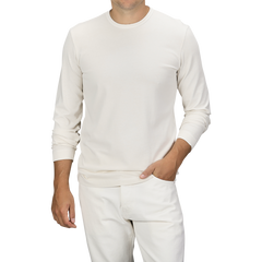 A person wearing an Ecru White Heavy Organic Cotton LS T-Shirt and white pants made of organic cotton from Tela Genova, standing against a plain background, with one hand in their pocket.