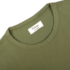 A close-up of a grass green heavy organic cotton long sleeve T-shirt by Tela Genova, featuring a white label that reads "Heritage" and "IZA LEANNA" inside the neckline.