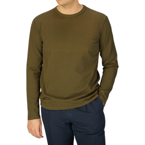 A man wearing a Military Green Heavy Organic Cotton LS T-Shirt by Tela Genova and navy blue pants against a grey background.