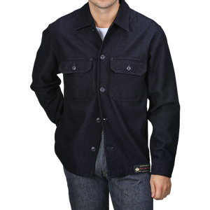 Dressed in the Tela Genova Navy Blue Wool Cotton Greto Overshirt and jeans, a person effortlessly exudes a sophisticated casual look, standing against a plain background.