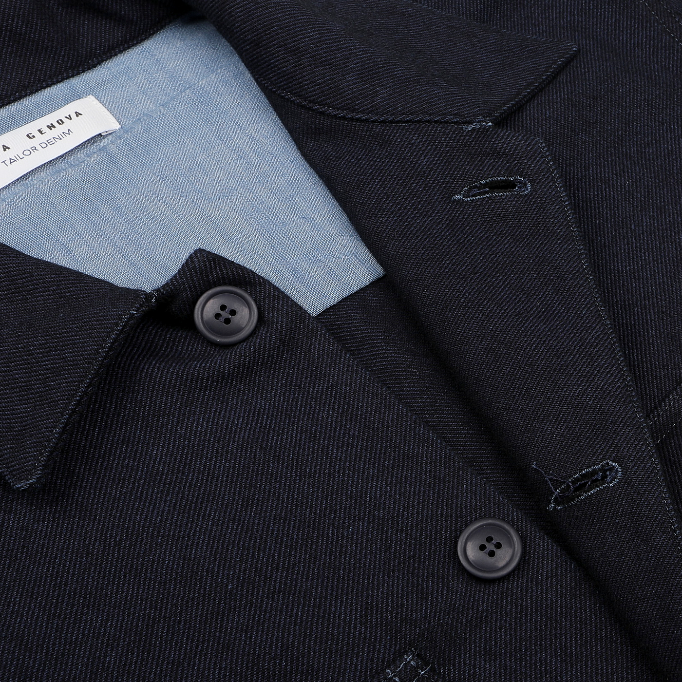 Close-up of the Navy Blue Wool Cotton Greto Overshirt by Tela Genova, showcasing a sophisticated casual design with two buttons and light blue lining. A white label on the inside seamlessly complements the wool-cotton twill fabric for enhanced comfort and style.