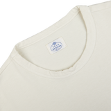 Close-up of a cream-colored Tela Genova Off-White Heavy Organic Cotton LS T-Shirt's neckline showing the Tela Genova brand label.