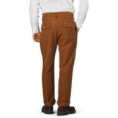 A person is standing with their back to the camera, dressed in Tela Genova's Tobacco Brown Cotton Moleskin Berardo Trousers, a crisp white shirt, and sleek black shoes.