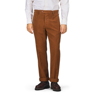 A person wearing Tela Genova's Tobacco Brown Cotton Moleskin Berardo Trousers, paired with a white shirt and brown shoes, stands against a plain background.