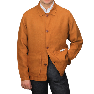 A person in a Tela Genova Tobacco Pure Linen Camillo Jacket featuring two front pockets and dark pants stands casually against a plain background.