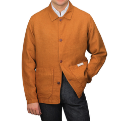 A person in a Tela Genova Tobacco Pure Linen Camillo Jacket featuring two front pockets and dark pants stands casually against a plain background.