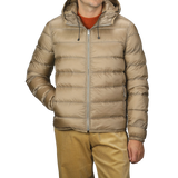 A person wearing a Ten C Beige Nylon Down Padded Liner Hood Jacket with a visible front zipper and their hands in the pockets. The jacket is paired with mustard-colored pants and a burnt orange sweater underneath.