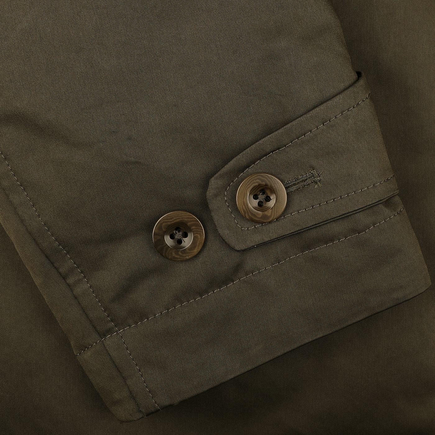 Close-up of the Green Technical Rainstorm Parka by Ten C, showcasing a fabric sleeve in khaki with a buttoned cuff. It features two brown buttons, visible stitching, and is crafted from waxed material for enhanced protection.