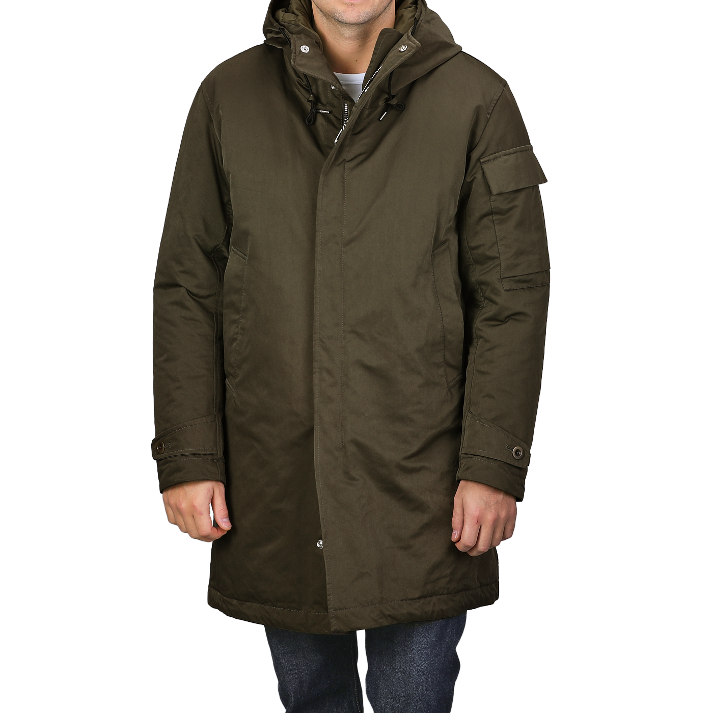 A person is wearing a knee-length Green Technical Rainstorm Parka by Ten C, crafted from waxed material, featuring a hood and snap closures.