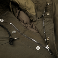 Close-up of the Ten C Green Technical Rainstorm Parka featuring a partially open silver zipper and black drawstring. Snap buttons line one side of the zipper, revealing its polyester and polyamide interior lining.