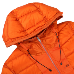 Close-up of the "Orange Nylon Down Padded Liner Hood Jacket" by Ten C. This technical outer nylon jacket features a front zipper, black drawstrings on the hood, and goose down padding for ultimate warmth.