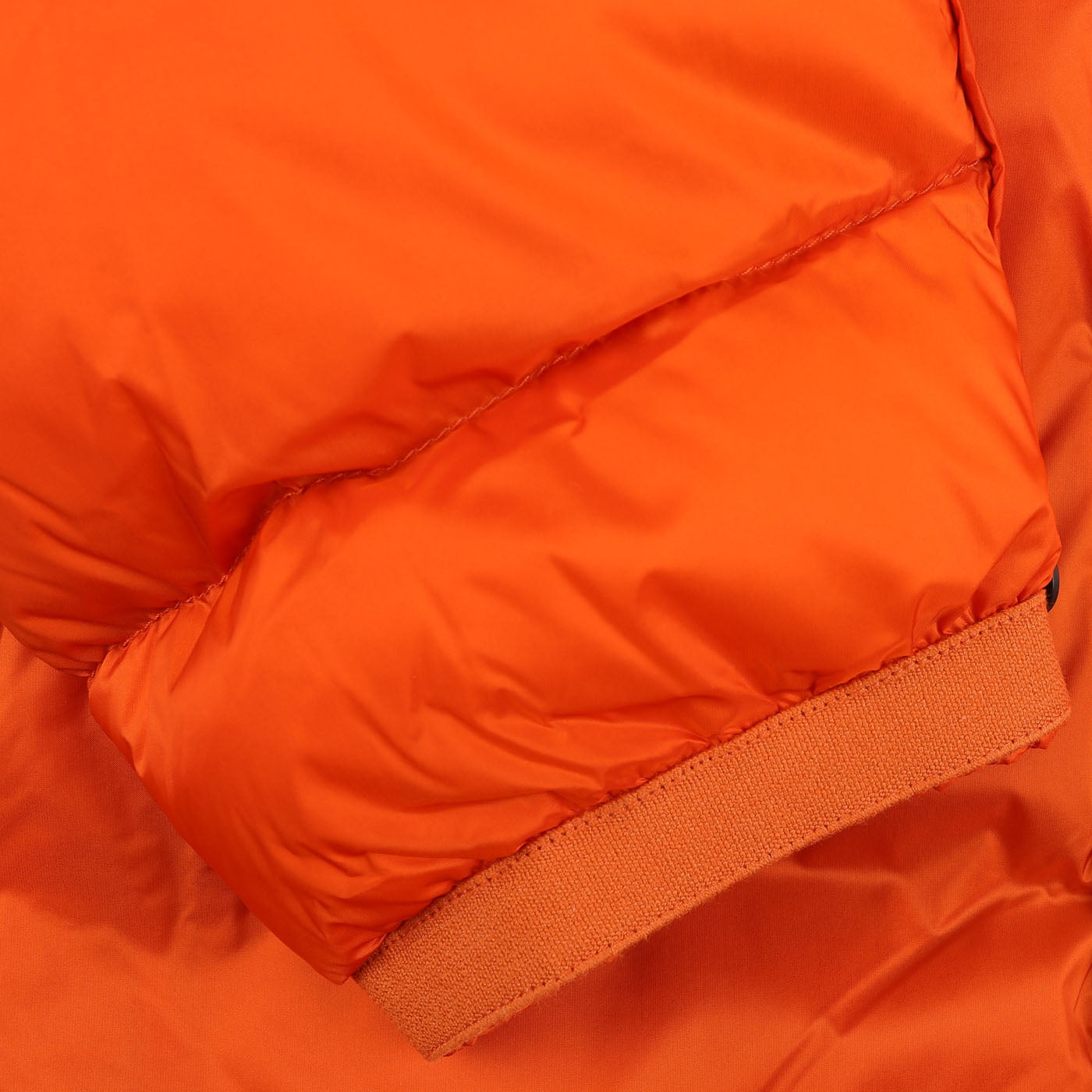 Close-up of a Ten C Orange Nylon Down Padded Liner Hood Jacket sleeve showcasing its quilted texture, ribbed cuff, and technical outer nylon with goose down padding.