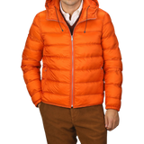 A person wearing an Orange Nylon Down Padded Liner Hood Jacket by Ten C over a white collared shirt and maroon sweater, paired with brown pants.