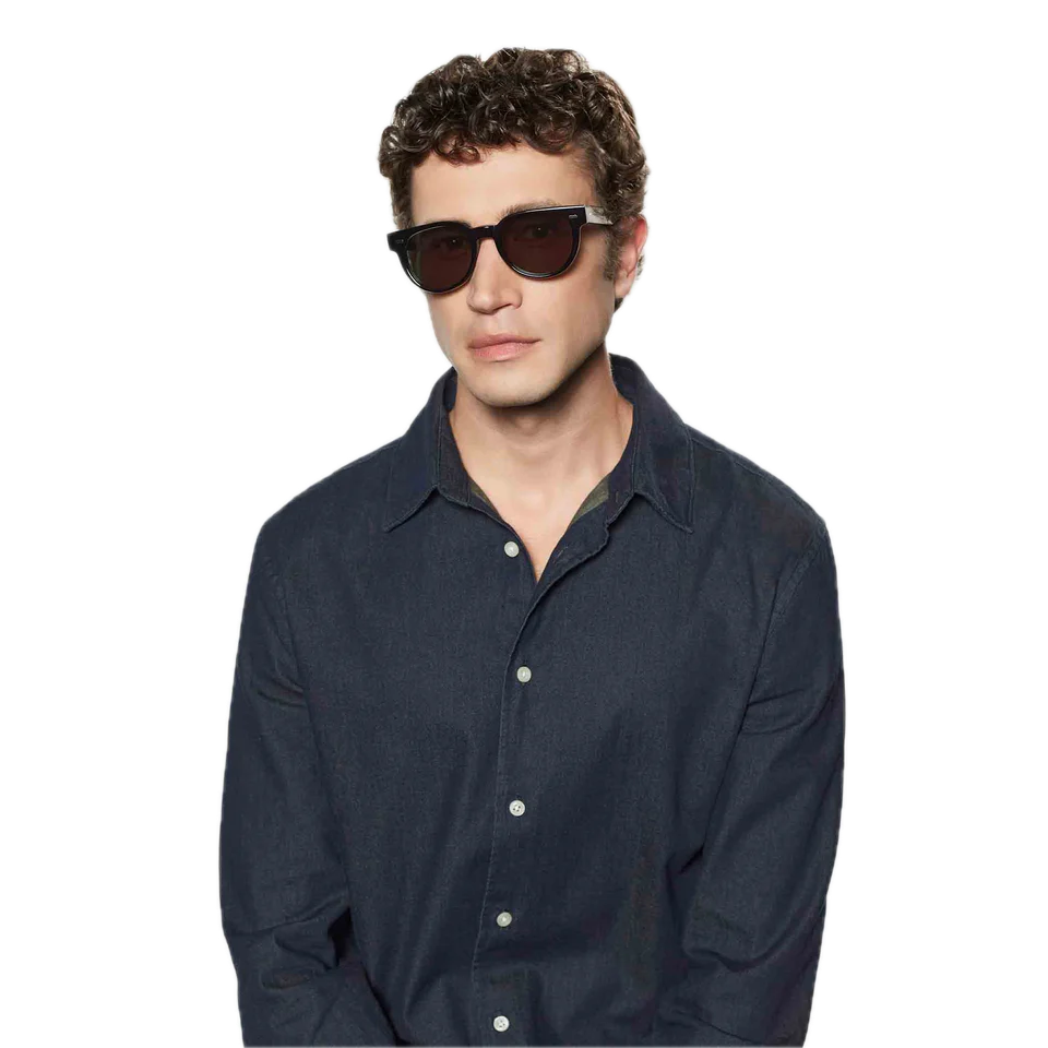 A young man wearing round-shaped, The Bespoke Dudes Palm Eco Black Green Lenses 51mm sunglasses and a navy blue shirt against a black background.