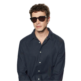 A young man wearing round-shaped, The Bespoke Dudes Palm Eco Black Green Lenses 51mm sunglasses and a navy blue shirt against a black background.