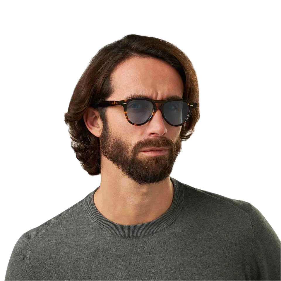 Man with long hair wearing sunglasses in the Piquet Eco Dark Havana Blue Lenses 49mm aviator model by The Bespoke Dudes and a gray sweater.