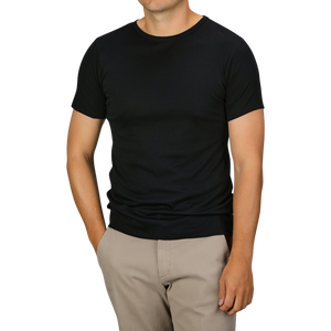 A person is standing, wearing a Black Pima Cotton Earth T-Shirt from The White Briefs and beige pants, with their hands resting in their pockets.